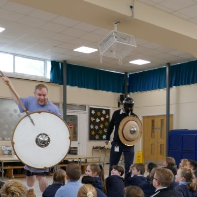 Ancient Greek presenter and our teacher in a helmet with a shield and spear with pupils in the foreground.